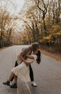 a man and woman kissing on the side of a road in front of some trees