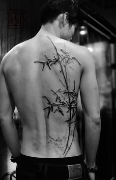 the back of a man's body is covered in bamboo leaves and has tattoos on it