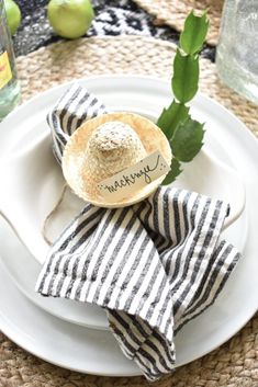 a white plate topped with a straw hat on top of a napkin next to an apple