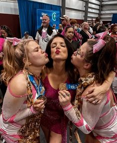 three women kissing each other in front of a group of people wearing pink and white