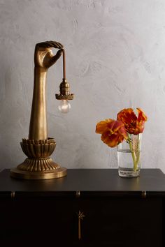 a vase with flowers and a golden lamp on a black table next to a white wall