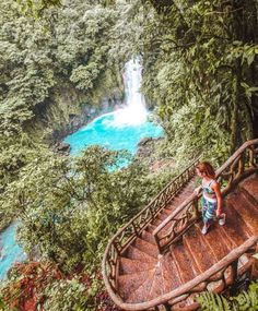 a woman standing on top of a wooden stair case next to a blue river in the forest