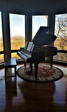 a grand piano sitting in the corner of a living room with large windows looking out onto a valley