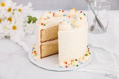 a slice is taken out of a vanilla cake with white frosting and sprinkles