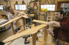 two men working on woodworking in a workshop, one holding a piece of wood