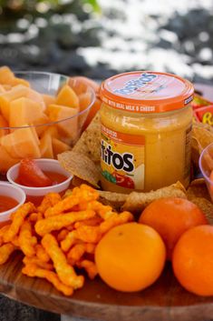 an assortment of fruit and crackers on a wooden platter next to bowls of dips