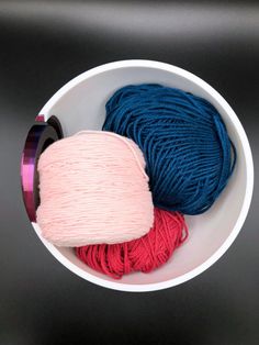 two skeins of yarn in a white bowl on a black surface, one blue and one pink