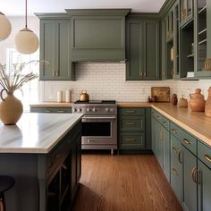 a kitchen with green cabinets and wood flooring is pictured in this image, there are two vases on the counter