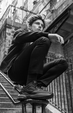 a young man sitting on top of a chair next to a stair case in front of a building