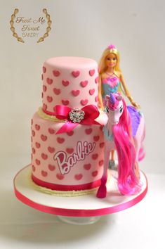 there is a pink cake with a pony on top and a barbie doll next to it