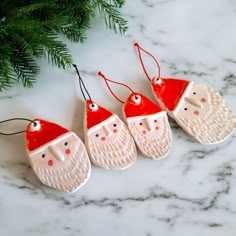 three ceramic santa claus ornaments hanging from a christmas tree ornament on a marble surface