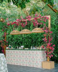 an outdoor bar with pink flowers and greenery on the wall, surrounded by plants