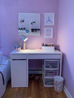 a white desk with drawers underneath it in a room that has purple walls and hardwood floors