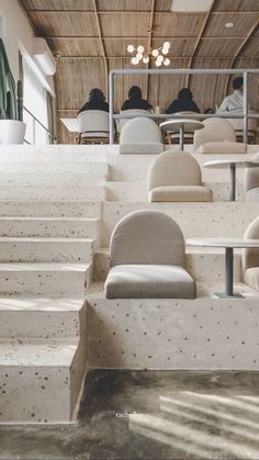 several people are sitting at tables and chairs in a room with concrete steps leading up to them