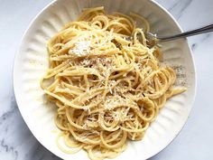 a white bowl filled with pasta covered in parmesan cheese on top of a marble counter