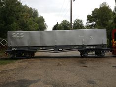 a train car sitting on top of a gravel road next to a red and yellow truck