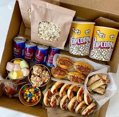 a box filled with lots of food next to two cans of popcorn and other snacks