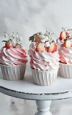 four cupcakes with pink frosting and strawberries on top are sitting on a cake stand