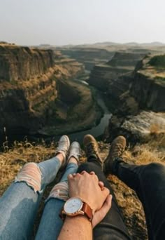 two people sitting on the edge of a cliff with their feet up in the air