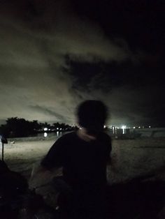 the man is riding his bike on the beach at night with dark clouds in the background