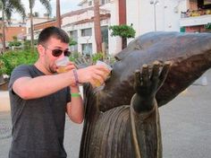 a man standing next to a statue drinking from a cup