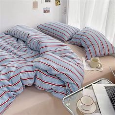 a laptop computer sitting on top of a bed covered in blue and red striped sheets