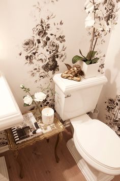 a white toilet sitting in a bathroom next to a wall with flowers on it's side