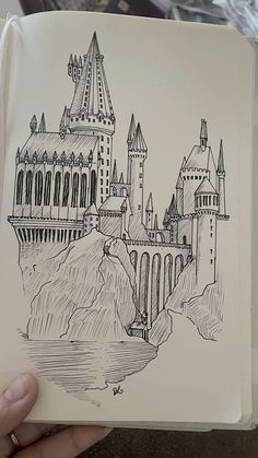 a drawing of a castle on a book in someone's hand with a pen