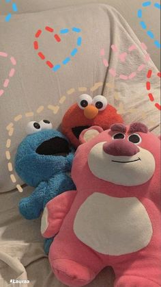 three stuffed animals sitting on top of a bed next to each other, one is blue and the other is red