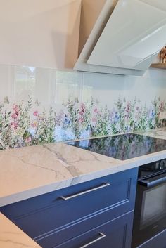 a kitchen with blue cabinets and flowers on the backsplash, along with a marble counter top