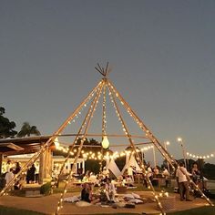 a group of people sitting in front of a tent with string lights on the roof