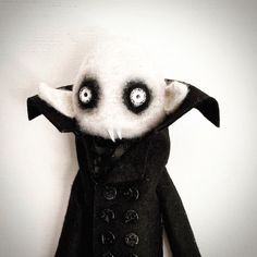 a black and white stuffed animal with eyes on it's head wearing a coat