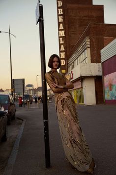 a woman standing next to a street sign on the side of a road with buildings in the background