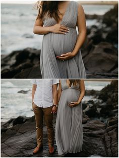 a pregnant couple holding hands and standing on rocks by the ocean with their belly wrapped around each other