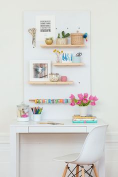 a white desk topped with shelves filled with books and vases next to a chair