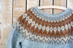 a sweater hanging on a wooden hanger next to a wood planked wall with an orange and white pattern