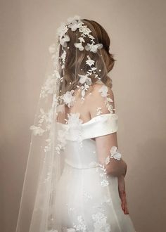 a woman wearing a wedding veil with white flowers on the back of her head and shoulder