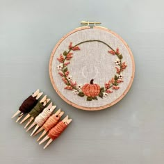 an embroidery kit with oranges and white flowers on it next to a wooden needle holder