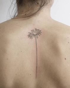 the back of a woman's shoulder with a single daisy tattoo on it