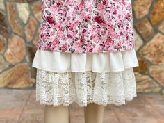 a woman's skirt with pink flowers and white lace on the bottom, in front of a stone wall