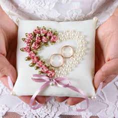 two hands holding a ring pillow with flowers and pearls on it