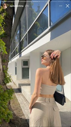 a woman standing in front of a tree with her hand on her head and wearing sunglasses