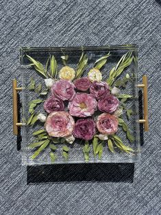 an arrangement of flowers is placed in a glass box on the ground, surrounded by leaves and twigs