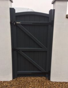 a black gate is open on the side of a white building with gravel in front of it