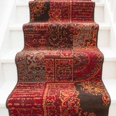 a carpeted stair case with red and black rugs on the bottom, next to white stairs