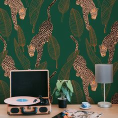 a desk with a record player, plant and wallpaper in the background that has leopards on it