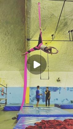 a woman is doing aerial tricks on a trampoline in an indoor gym with other people