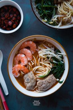 two bowls filled with noodles and shrimp next to chopsticks on a blue surface