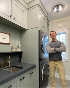 a man standing in a kitchen next to a washer and dryer with his arms crossed