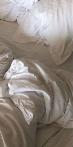 an unmade bed with white sheets and pillows